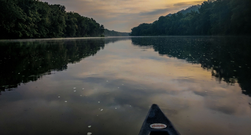 The tip of a canoe appears in the foreground, resting on calm water that reflects the sky.